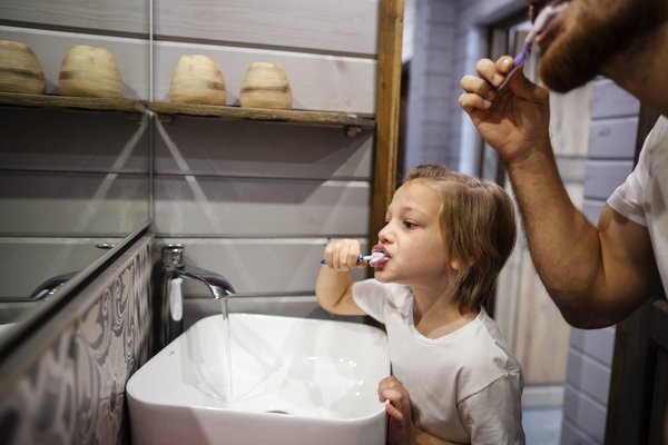 pai e filha escovando os dentes e deixando a torneira aberta